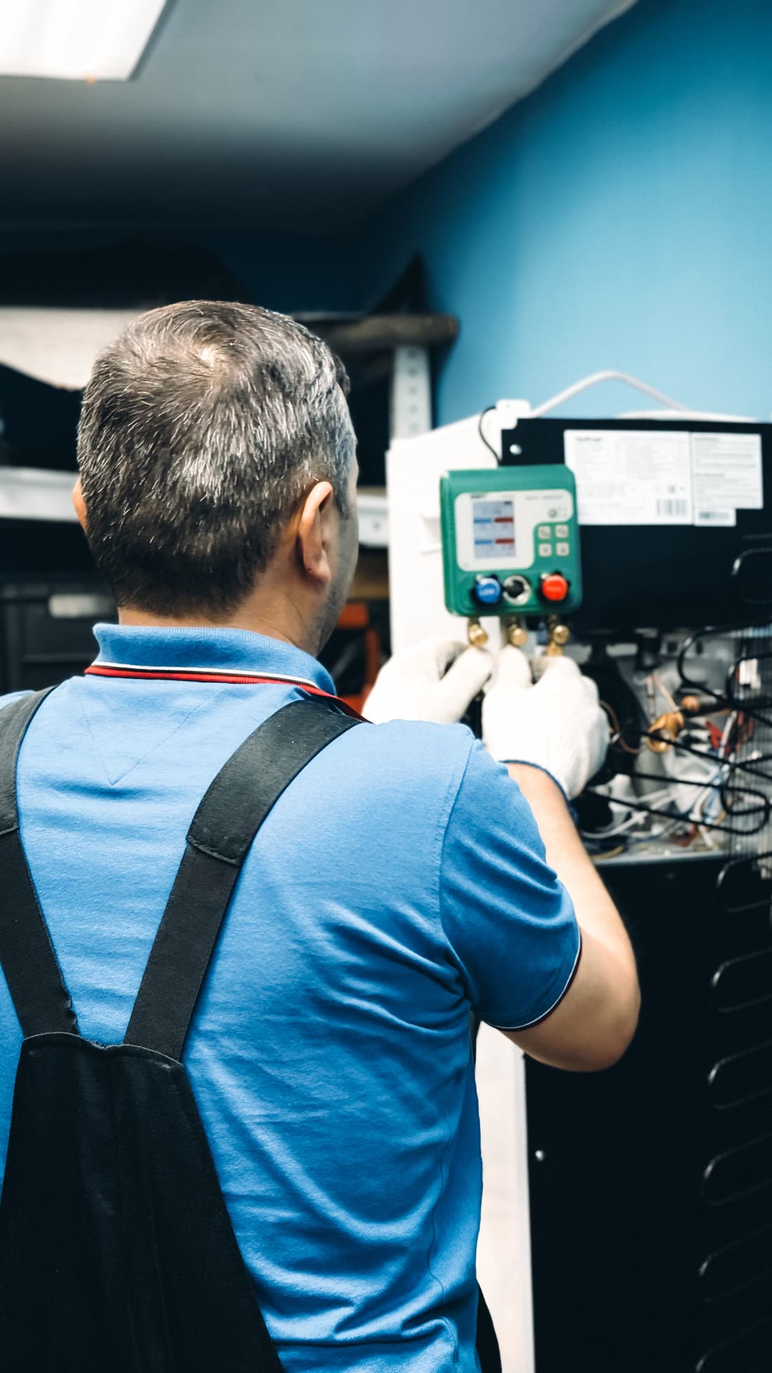 HVAC technician in gloves reading a digital manifold gauge on an air conditioning system
